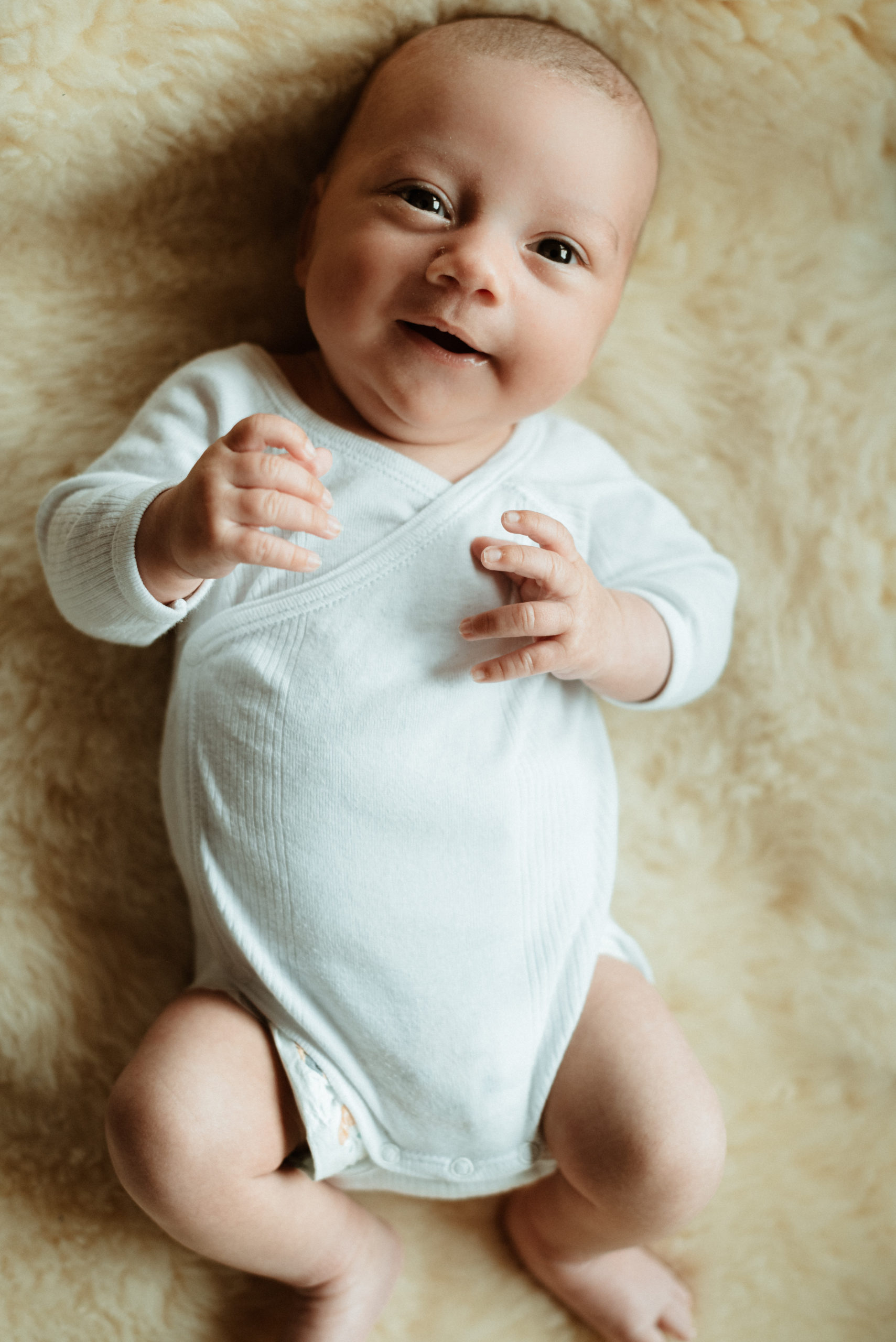 Wunderschöne Einzelaufnahme des Babies, wie es lächelnd in die Kamera schaut beim Neugeborenen Fotoshooting.